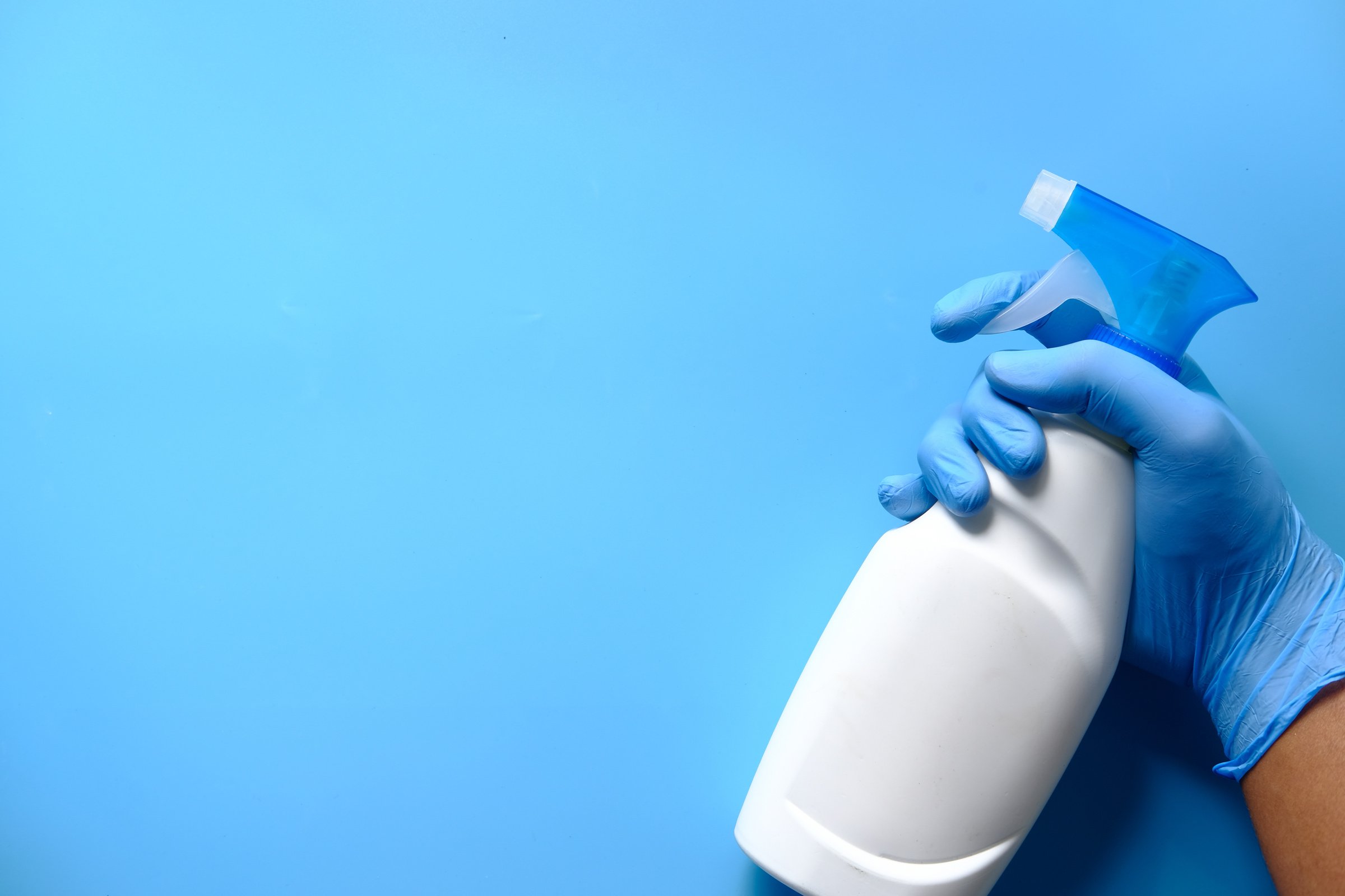 Hand in Blue Rubber Gloves Holding Spray Bottle with Copy Space